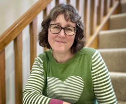 Author photo with a white woman with dark hair in a green top sitting on stairs