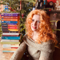Photo of a white woman with red hair next to a stack of books