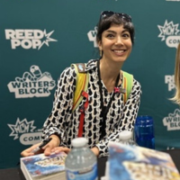 Photo of an author signing books in front of a logo'd background