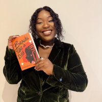 Image of a Black woman holding an orange book against a white wall