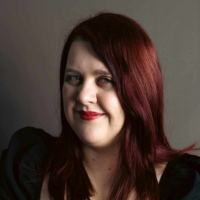 Author headshot of a white woman with red hair in a black top