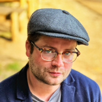 Headshot of a white man in a newsboy cap