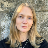 Headshot of white woman with blonde hair against a stone wall
