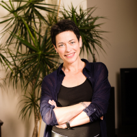 headshot of a white woman with short dark hair against a houseplant