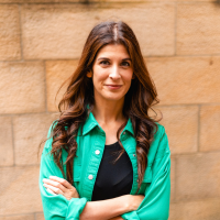 Photo of a white woman with loose brown hair and a green shirt in front of a brick wall