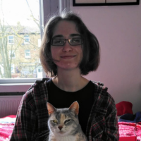 Image of a white person with dark hair and a cat on their lap