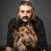Photo of a white woman with dark hair and a fake moustache and a big brown dog