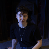 Headshot of a white person in a dark top in a dark room