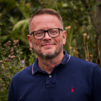 headshot of a white man in a blue shirt against greenery