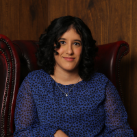 A south Asian woman, in a blue top sits in a red leather wingback chair