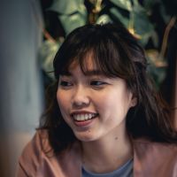Headshot of a Malaysian woman with loose brown hair with indoor plant behind