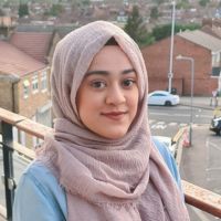 Headshot of a woman in a pink hijab on a balcony overlooking a road