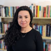 Headshot of a white woman with curly black hair against a bookcase