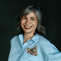 Headshot of a white woman in a blue shirt against a black backdrop